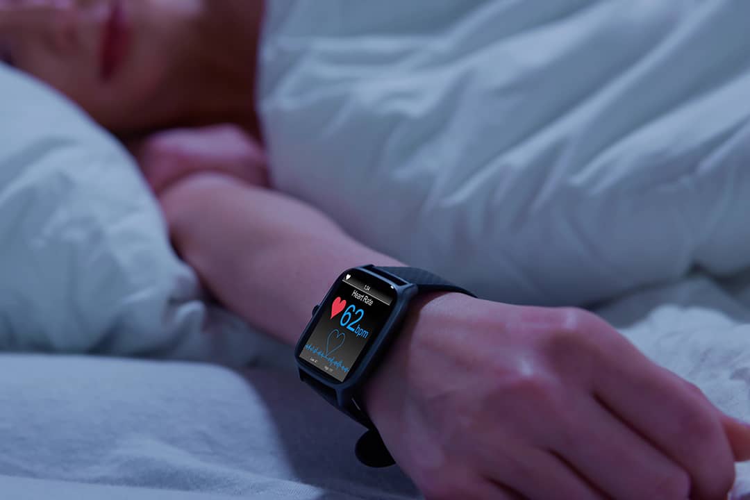 Person in bed wearing a smartwatch with heart rate monitor.